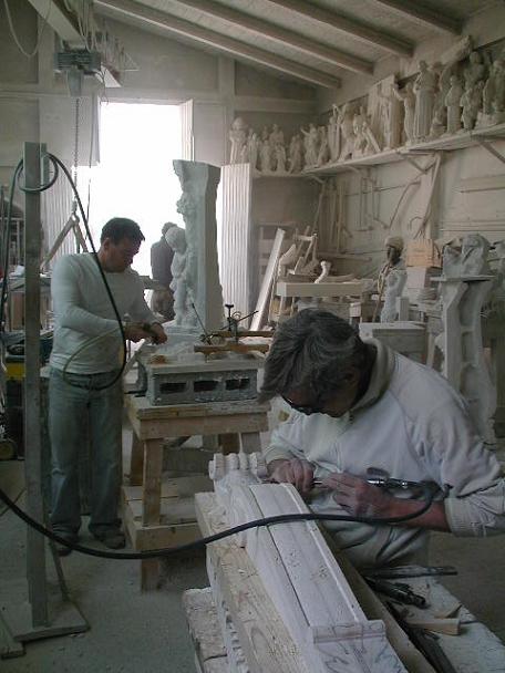 un escultor estudiante visitando nuestro taller y un artesano experto, tallando a mano partes de una chimenea